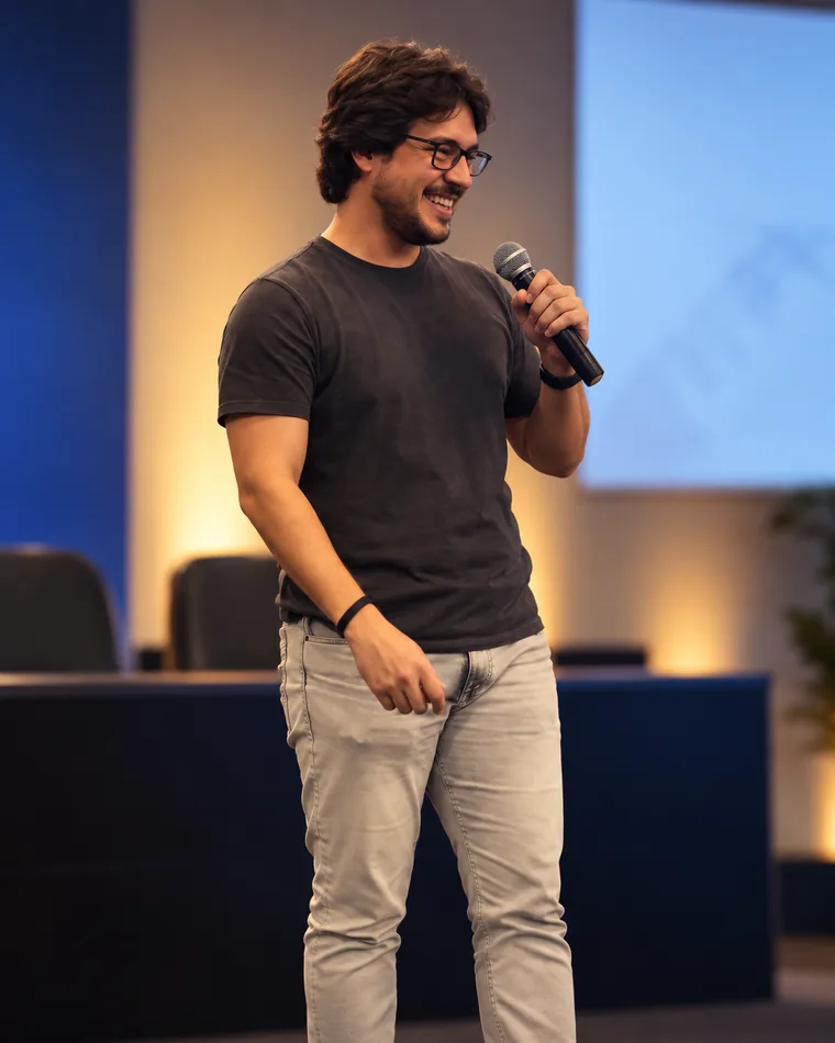 Bruno Gianolla sorrindo no palco, segurando um microfone